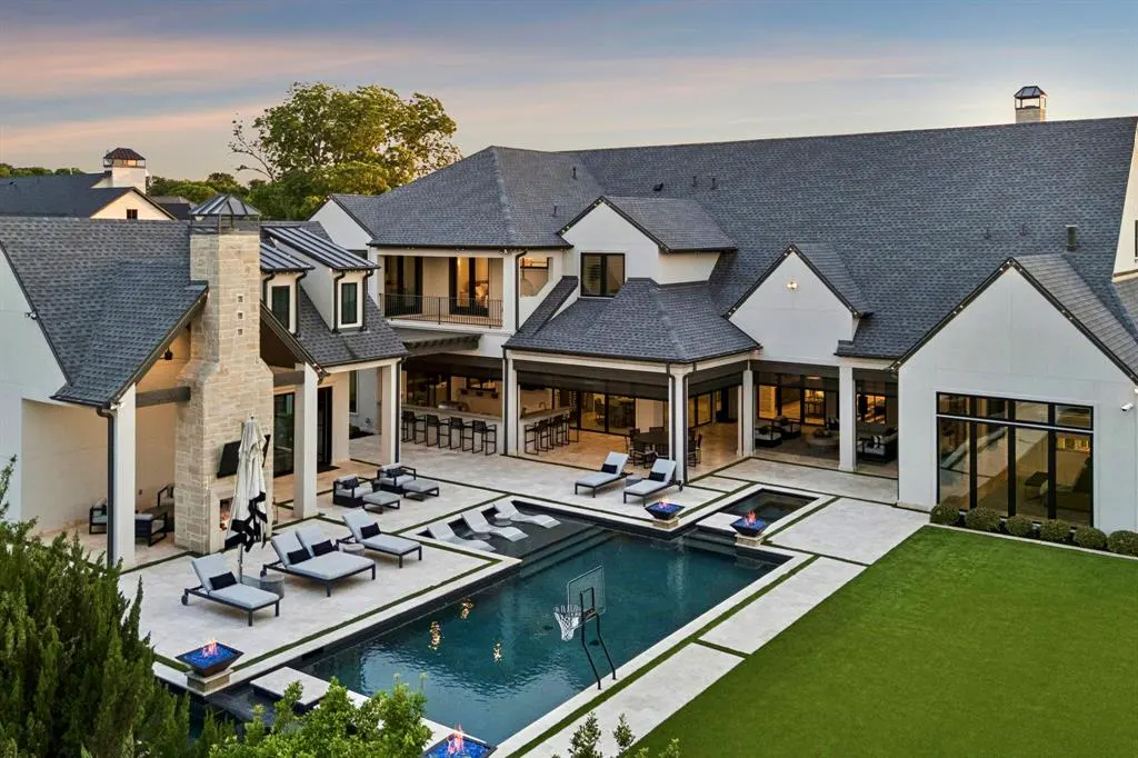 Aerial view of a large white house with a dark roof, pool, lounge chairs, and outdoor kitchen.
