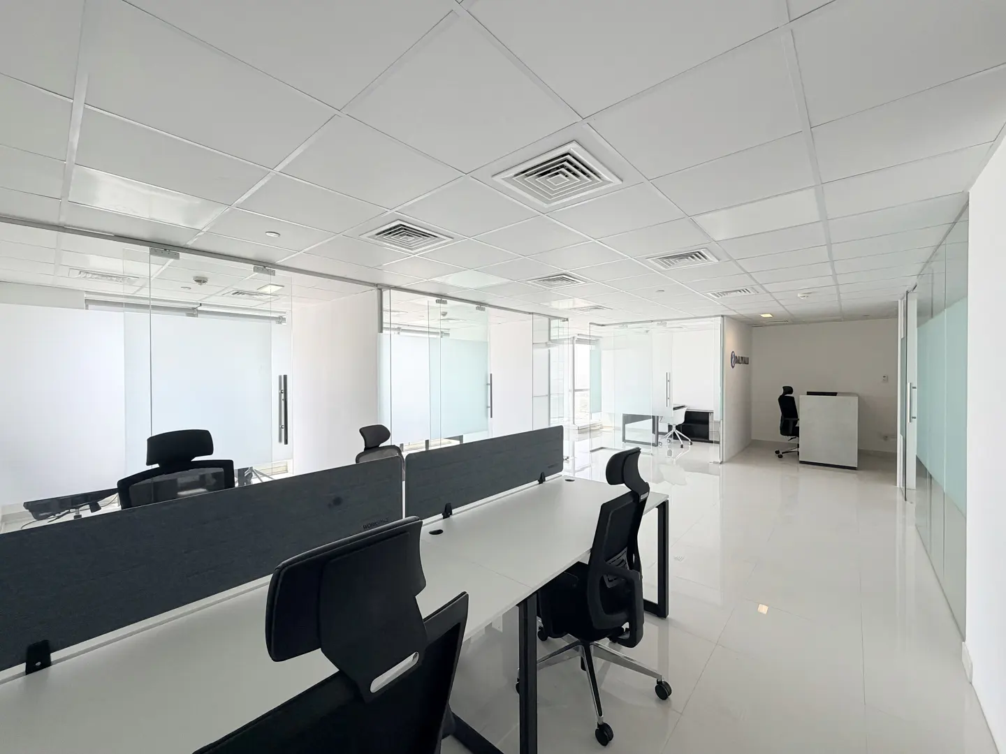 Bright, modern office space with white desks, black chairs, and glass-walled offices.