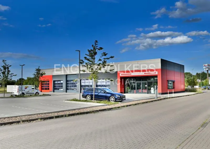 Engel & Völkers commercial building with red accents, garage doors, and a blue car parked in front on a sunny day.