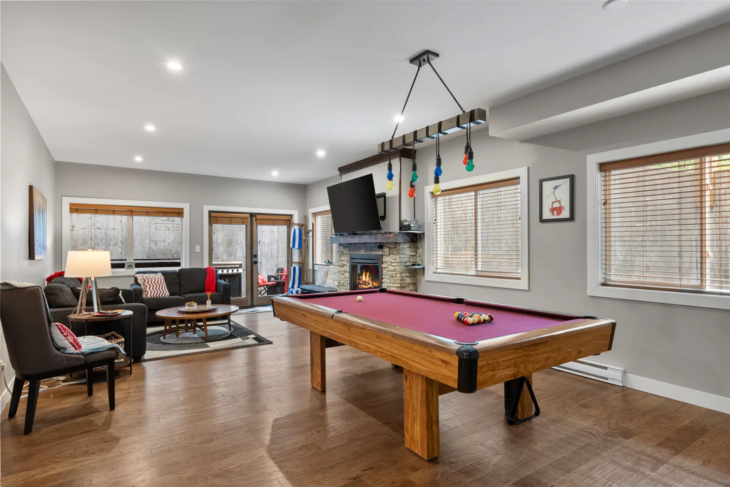 A game room with a wooden pool table, a fireplace with a mounted TV, and a seating area with a sofa and armchair.