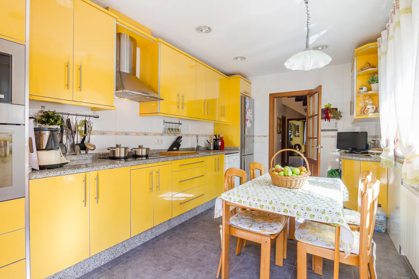 Bright kitchen with vibrant yellow cabinets, granite countertops, and a dining table with a fruit basket.