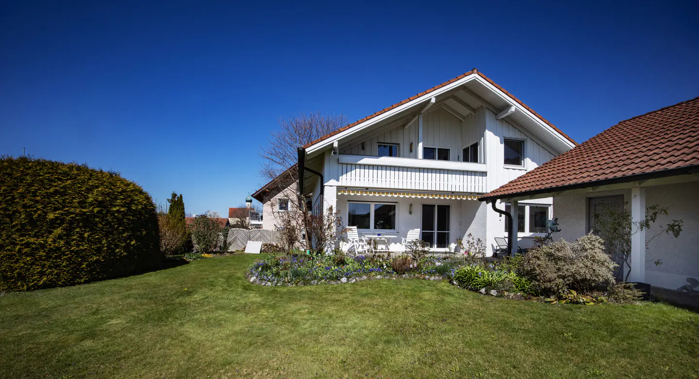 Two-story white house with a red tile roof, green lawn, and blue sky.