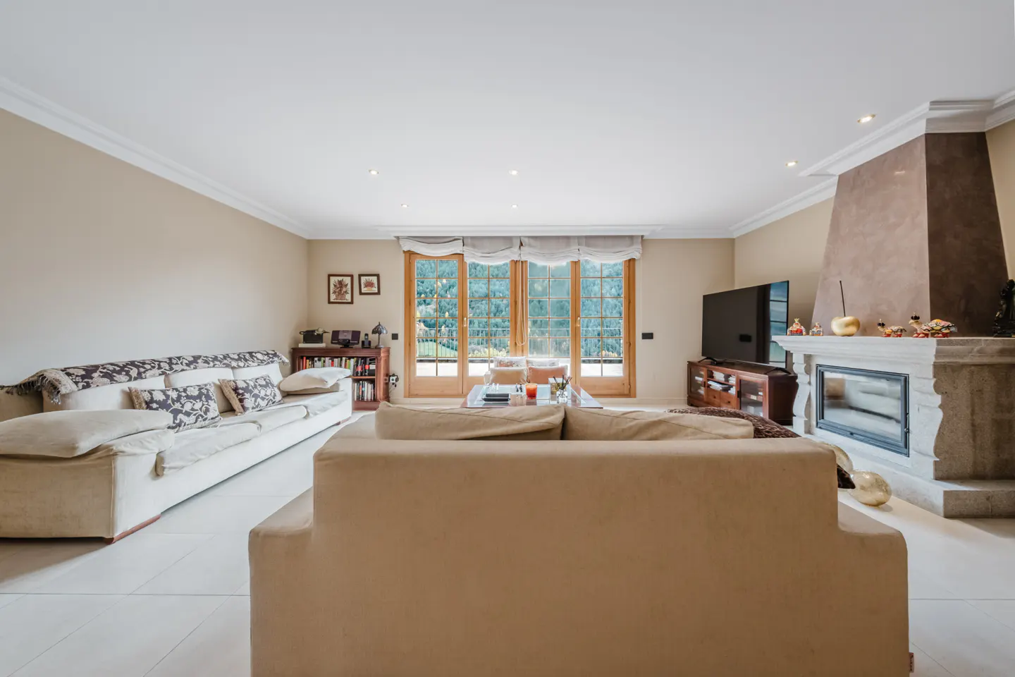 Bright living room with beige walls, two sofas, a fireplace, a TV, and a glass door to the outside.