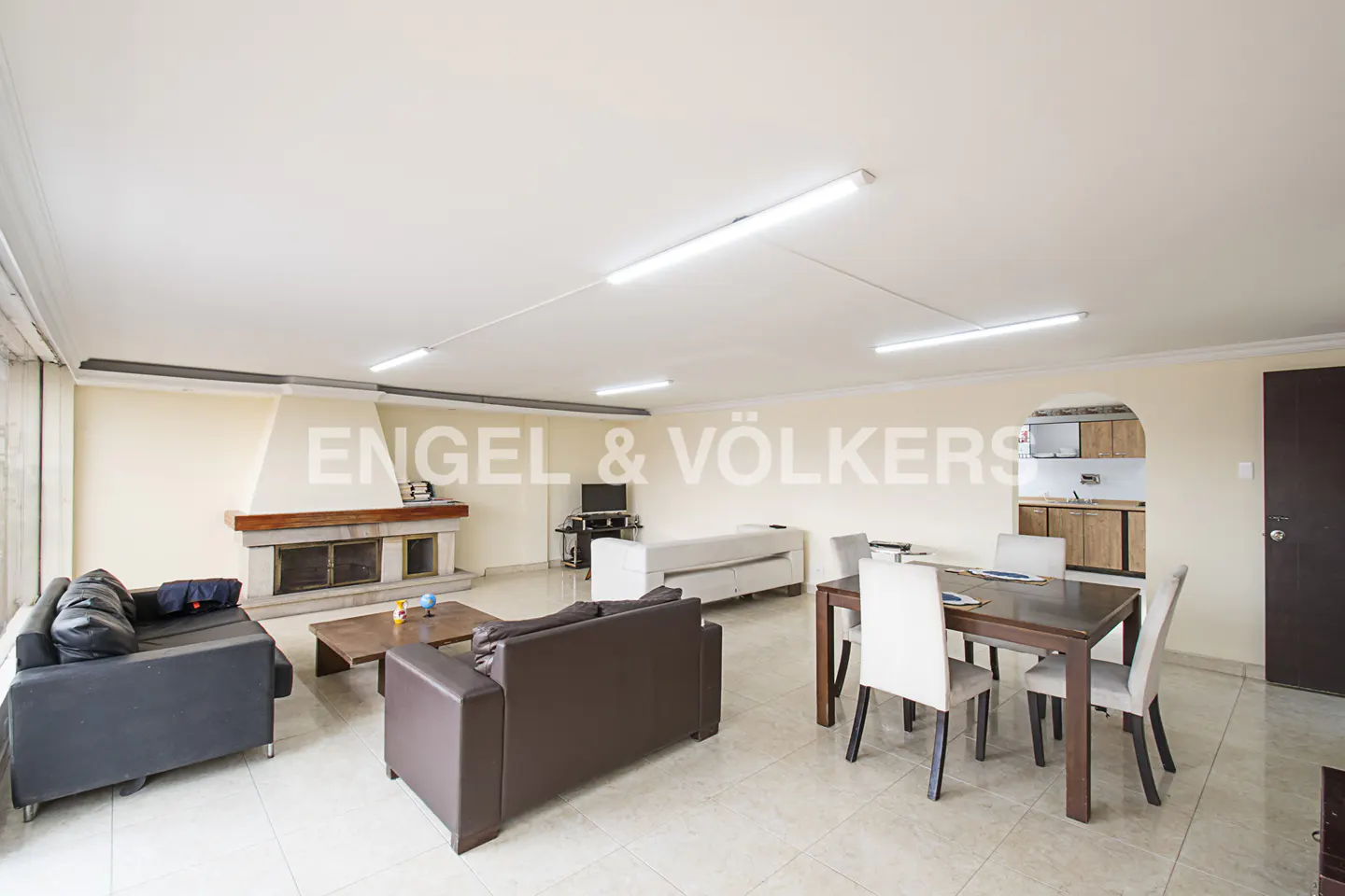 A bright, open-plan living and dining area with a fireplace, sofas, and a dining table with white chairs.