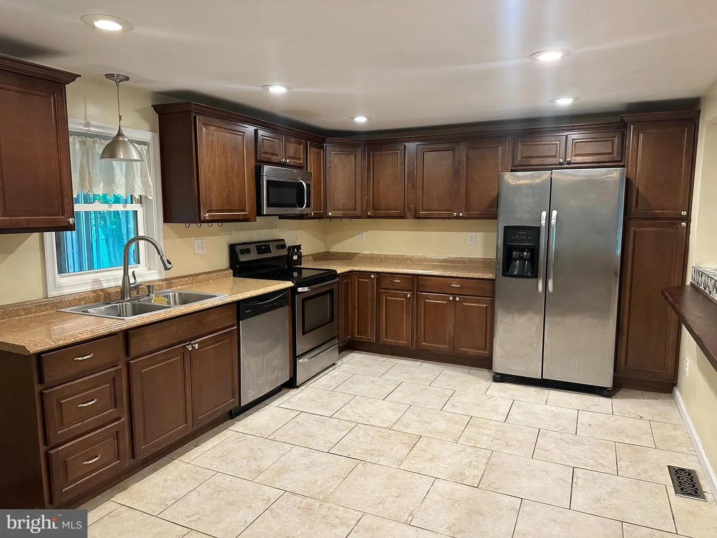 A kitchen with brown cabinets, stainless steel appliances, and beige tile flooring.