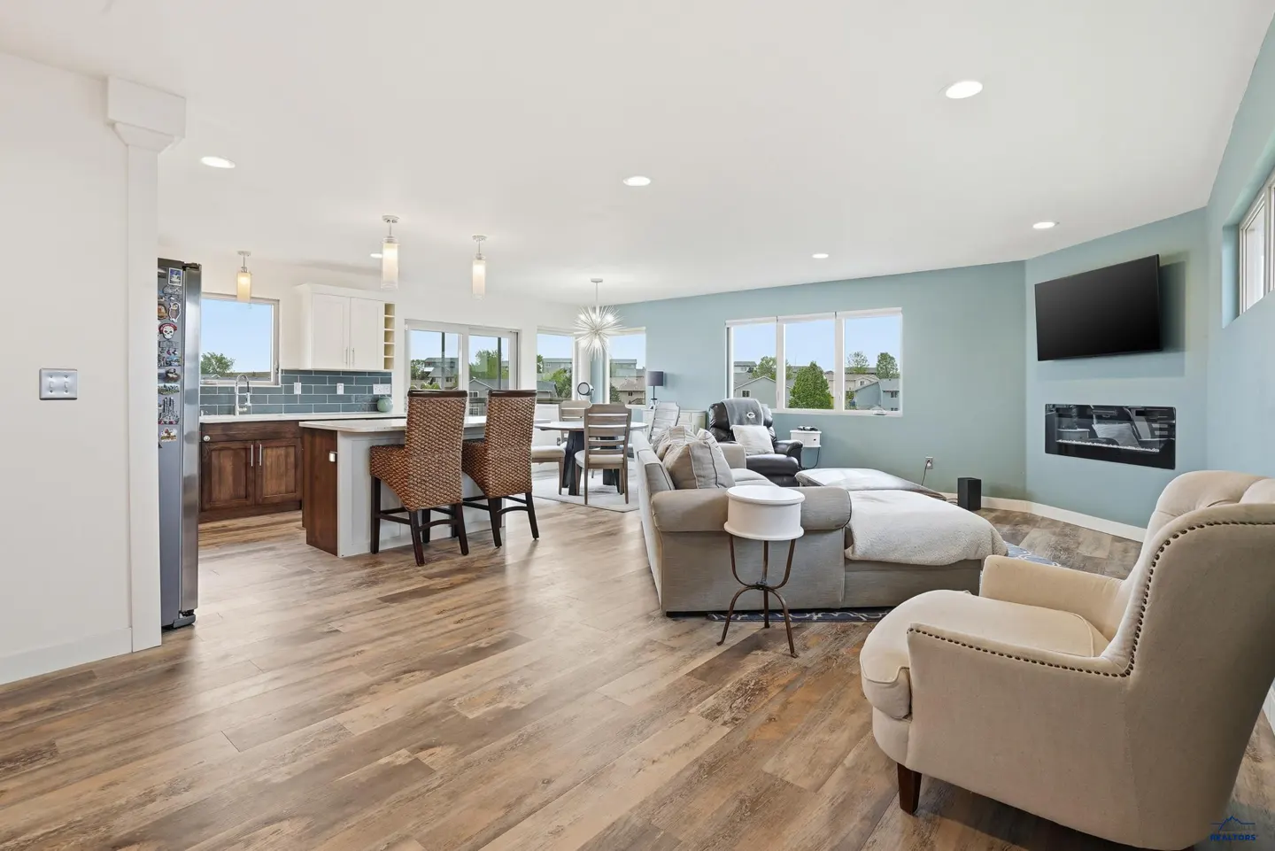 Open-concept living area with a kitchen, dining space, and light blue walls, featuring a sectional sofa and accent chair.