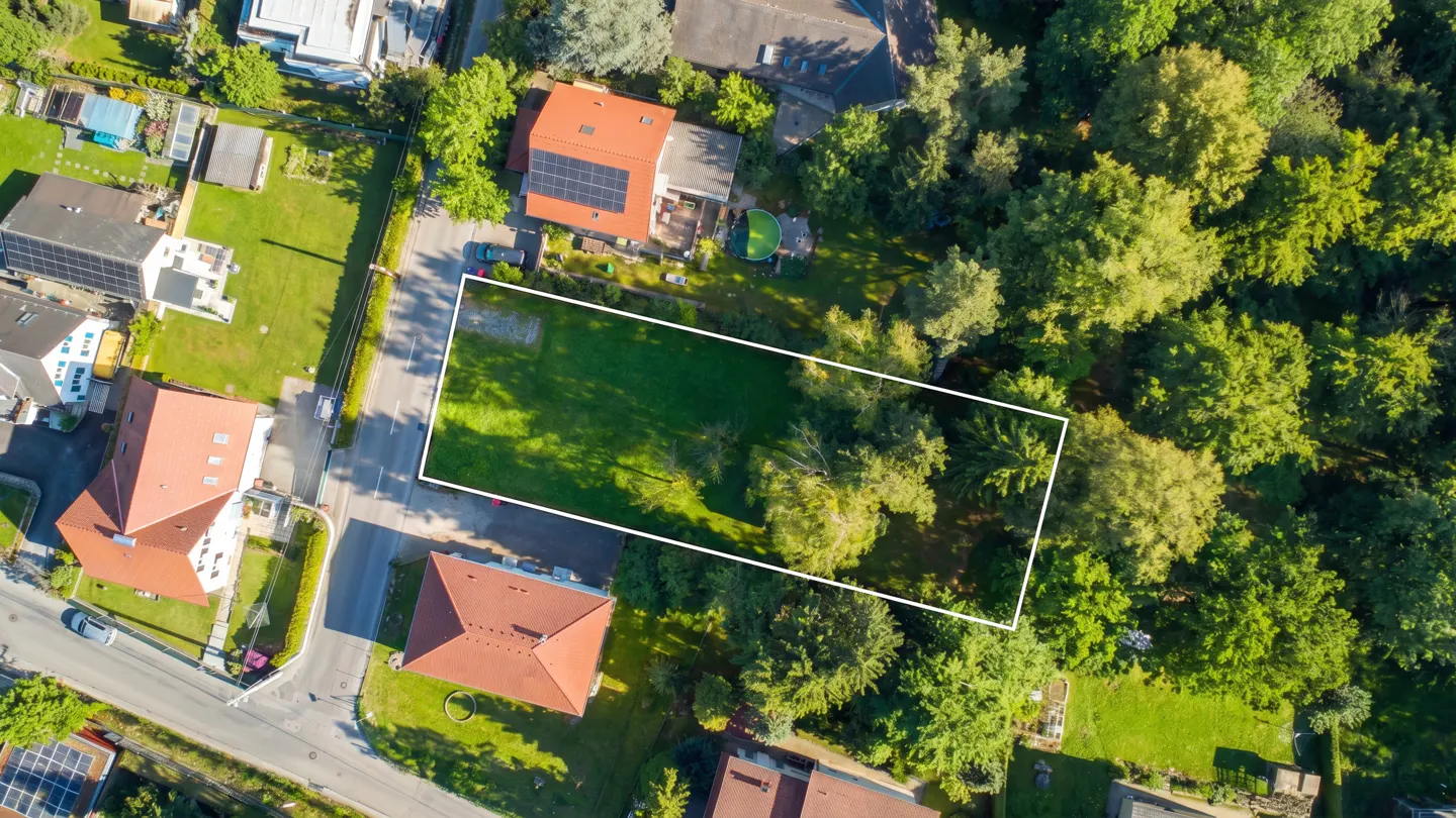 Aerial view of a rectangular grassy lot outlined in white, surrounded by trees and houses with red roofs.