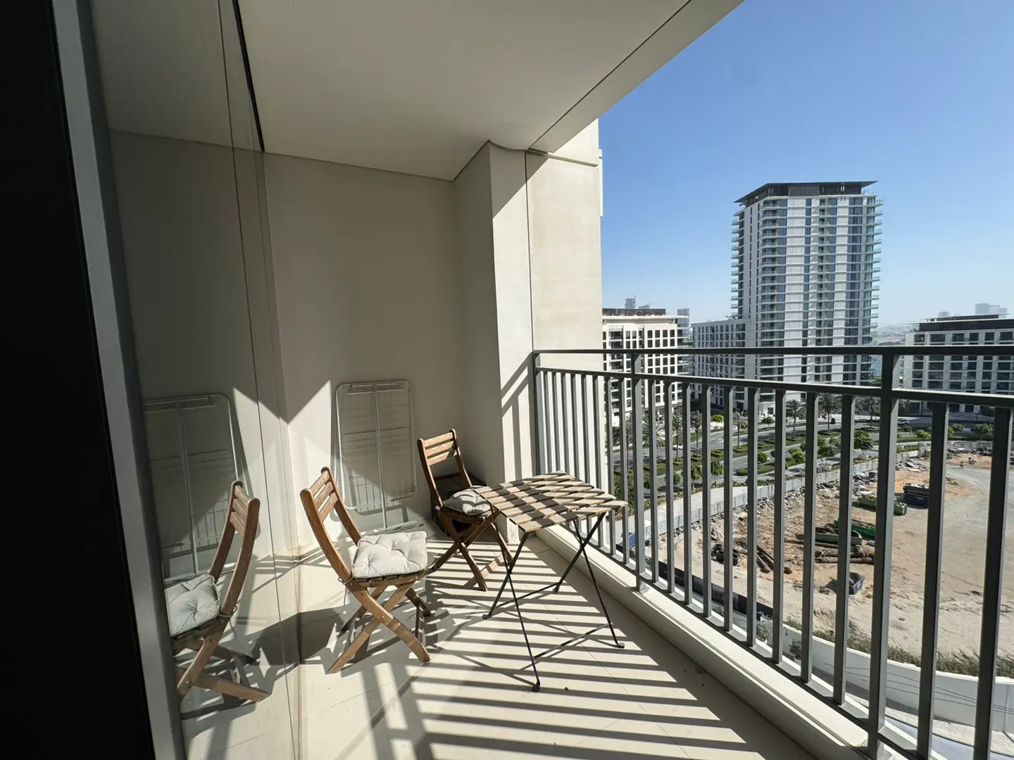 Balcony with a table and two chairs, overlooking a city skyline on a sunny day.
