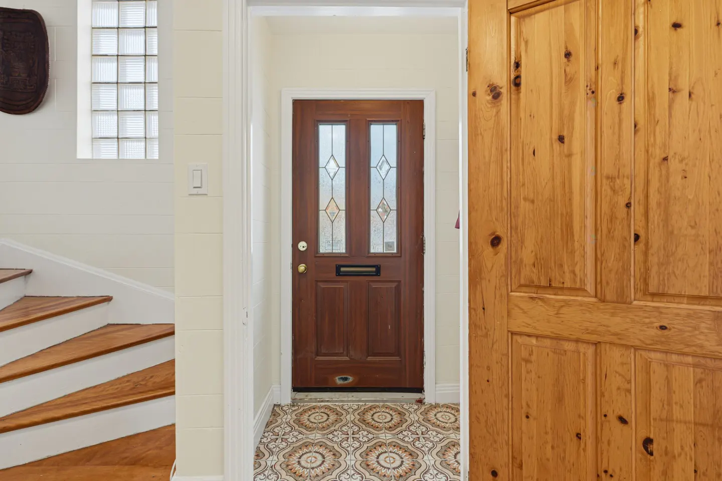 Interior view of a home's entryway with a wood door, patterned tile floor, and staircase.