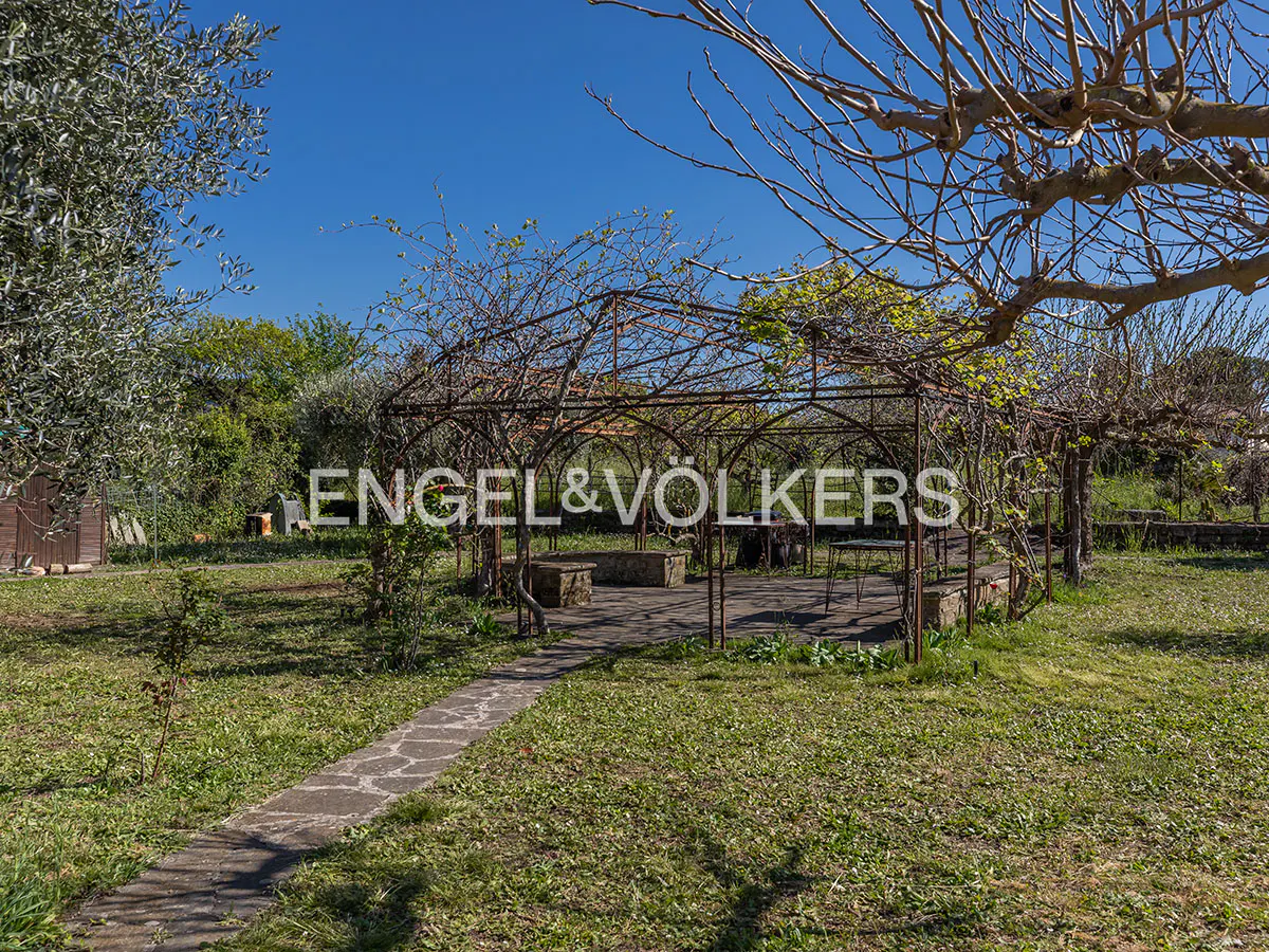 A garden with a metal gazebo, stone benches, and a stone path under a blue sky. The Engel & Volkers logo is superimposed on the image.