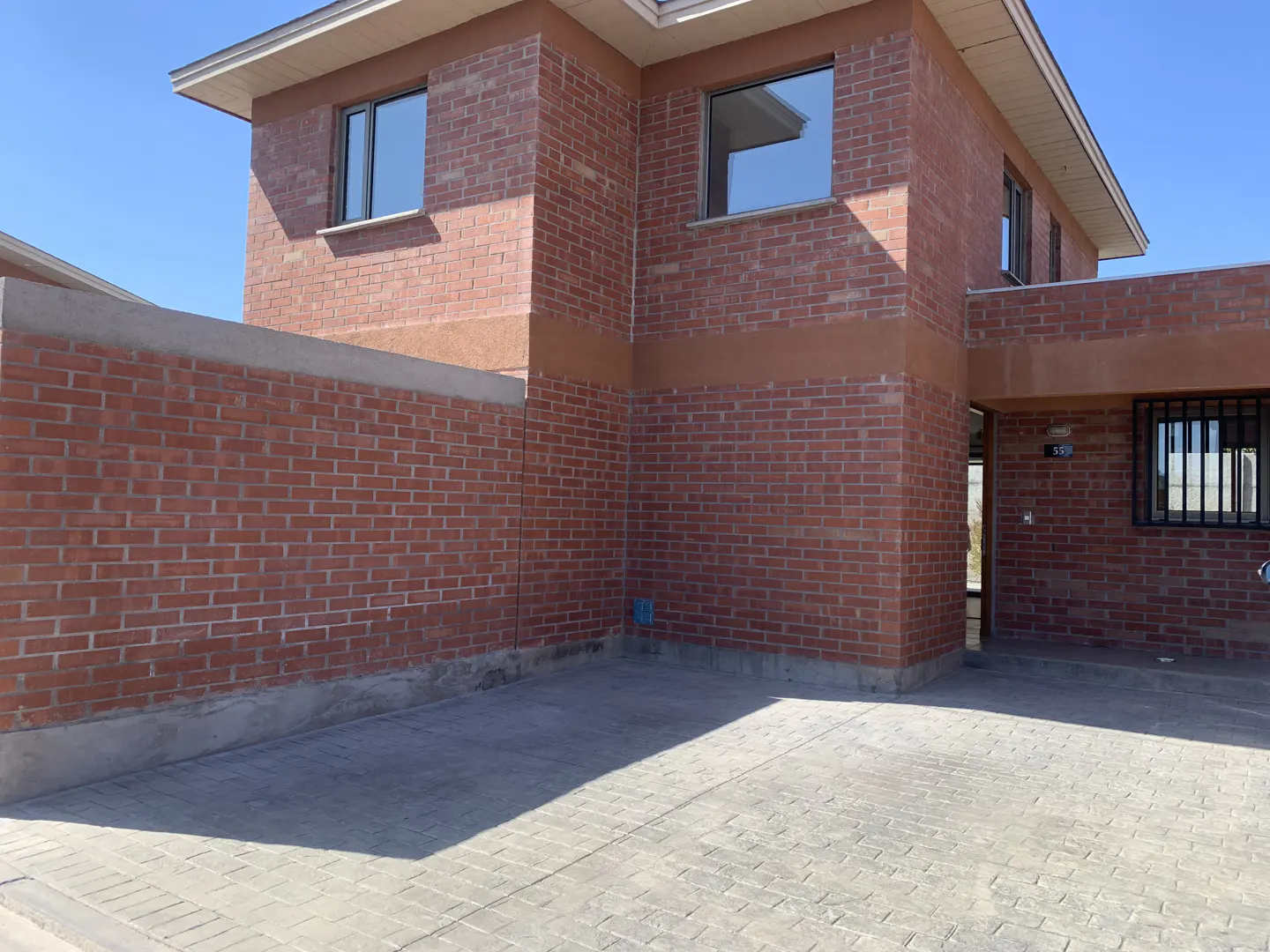 Exterior view of a two-story brick house with a brick privacy wall and a concrete driveway on a sunny day.