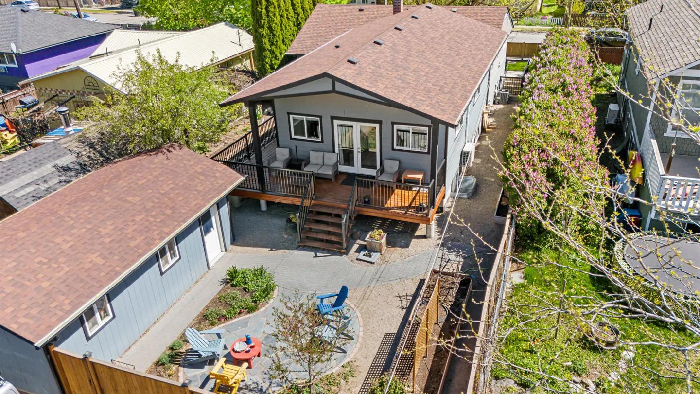Aerial view of a gray house with a brown roof, a wooden deck, and a backyard with colorful chairs.