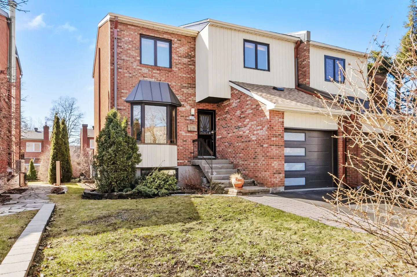 A two-story brick townhouse with a black garage door and a small front yard.