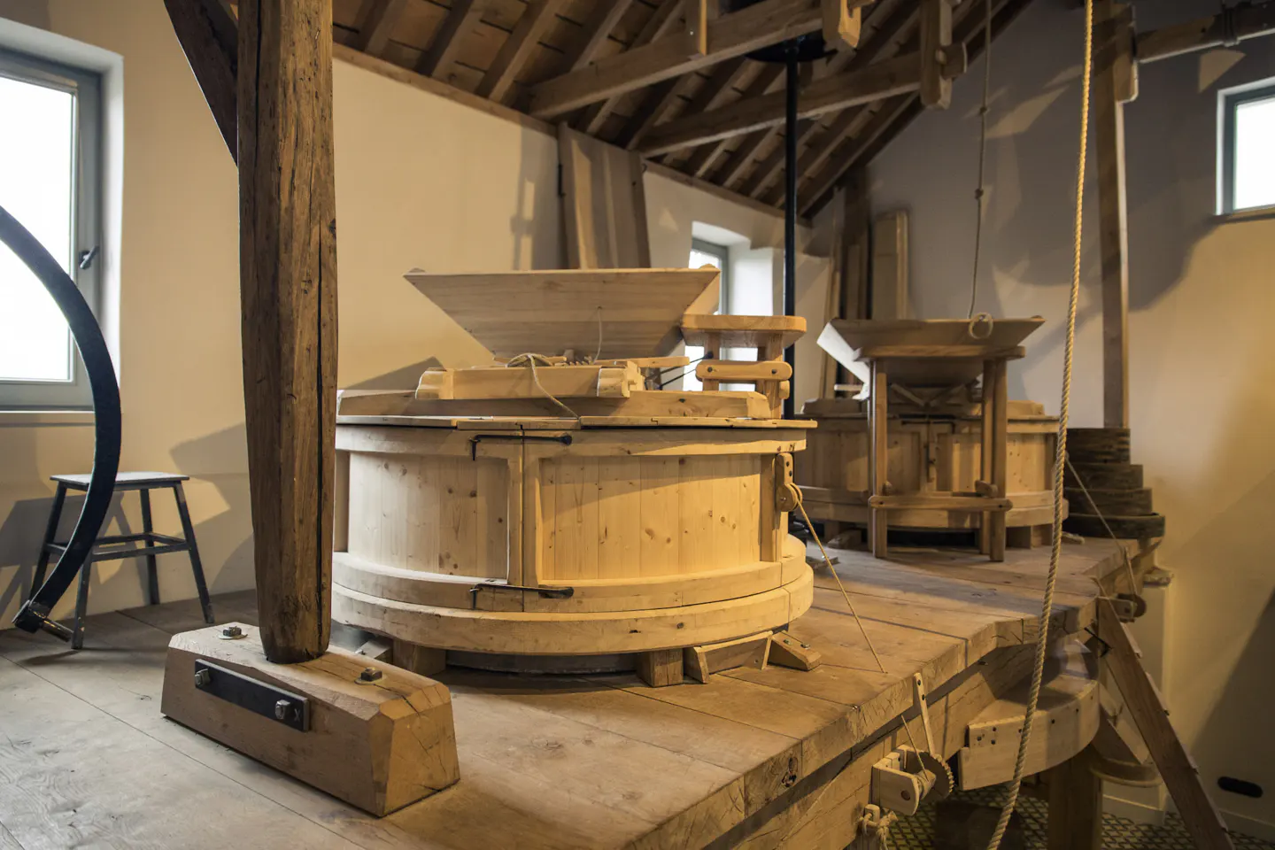 Interior view of a wooden mill with a hopper, beams, and a window.