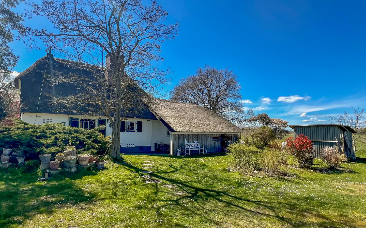 Exterior view of a white house with a thatched roof, green lawn, and blue sky.