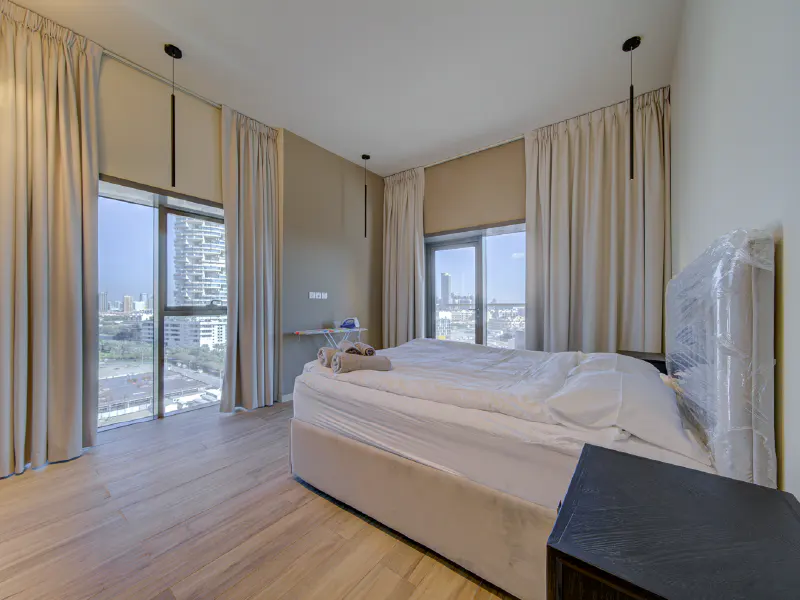 Bedroom with a bed, beige curtains, and a city view. Wood floors and black pendant lights add modern touches.