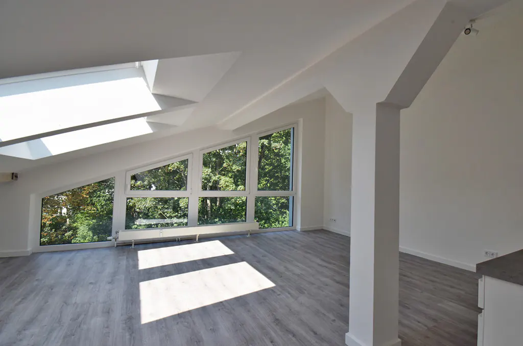 Bright, modern room with gray wood floors, white walls, and large windows overlooking green trees. Skylight in the ceiling.