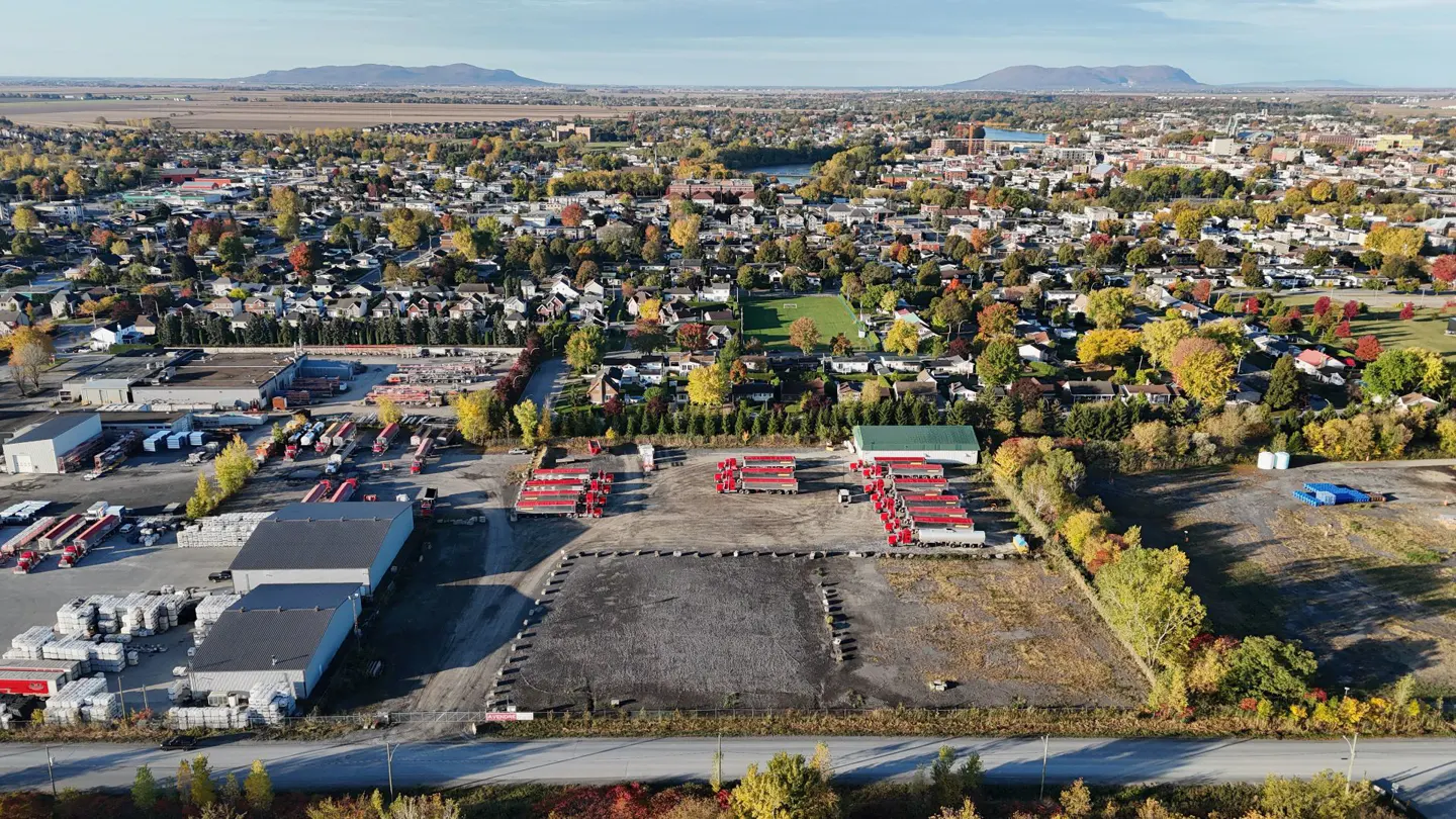 Aerial view of a town with mountains in the background, a commercial lot with red trailers, and gray buildings.