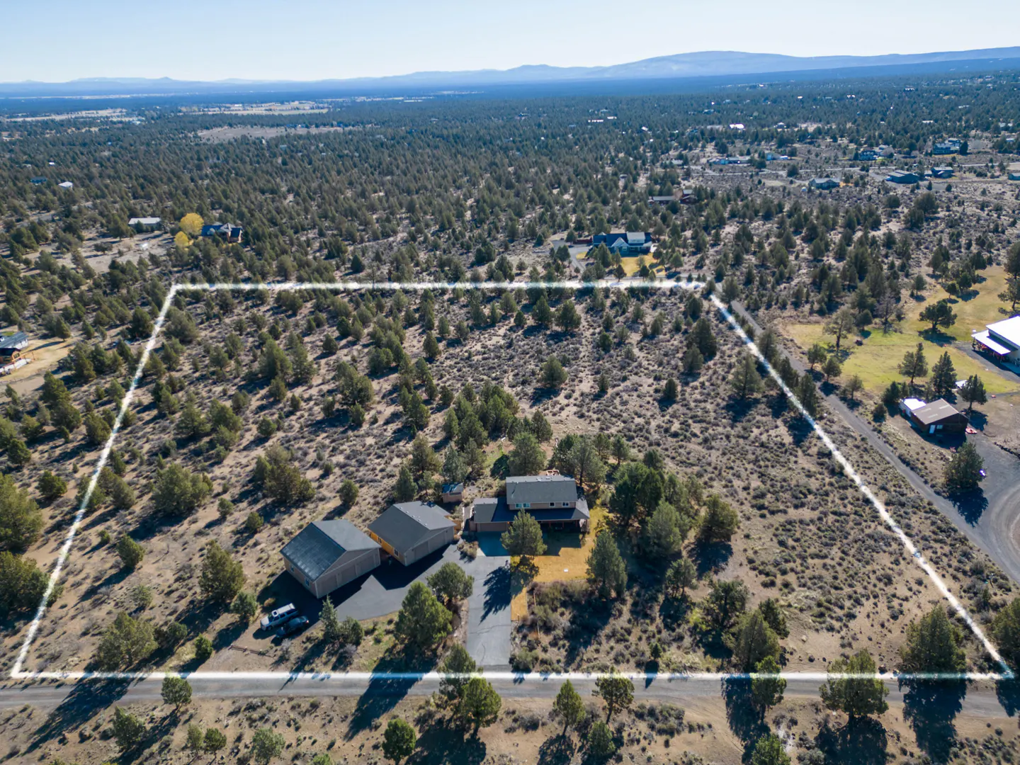 Aerial view of a property with a house, garage, and outlined land in a desert landscape with trees.
