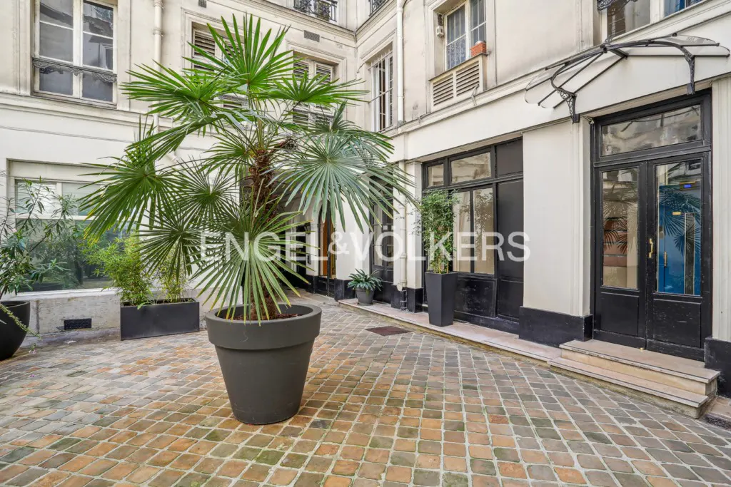 Courtyard view with palm tree in pot, brick floor, and building facade with black door and windows. Engel & Volkers logo visible.