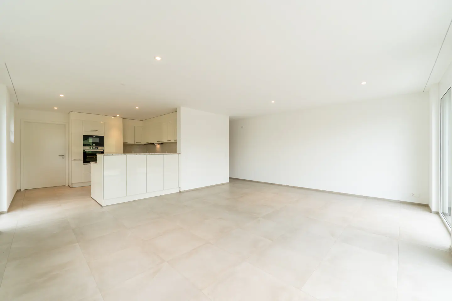 Modern, minimalist open-plan living area with white kitchen cabinets, light tile floors, and recessed ceiling lighting.