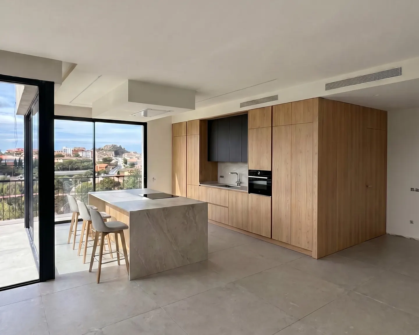 A modern kitchen with light wood cabinets, a gray island with four stools, and a large window with a city view.