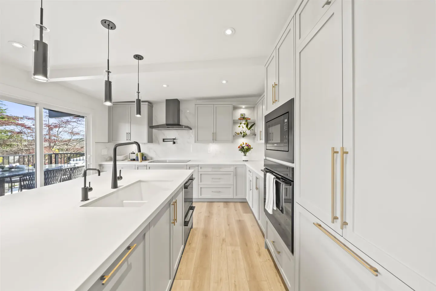 Bright, modern kitchen with white cabinets, island, black fixtures, and wood floors. A sliding glass door leads to an outdoor patio.