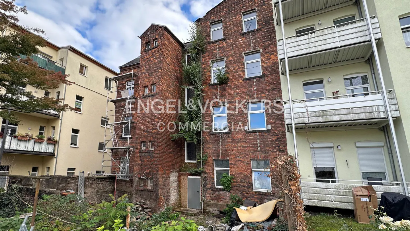 Exterior view of a red brick building with white windows, scaffolding, and an overgrown yard. Engel & Volkers logo visible.