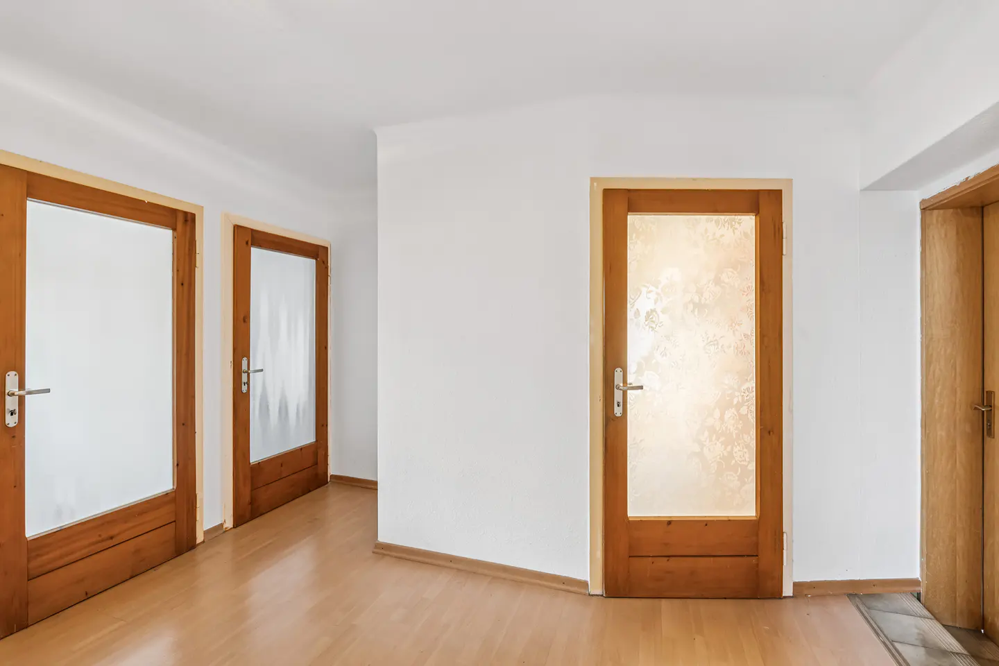 Bright hallway with three wooden doors, two with frosted glass, and a shiny wood floor. The walls are white.