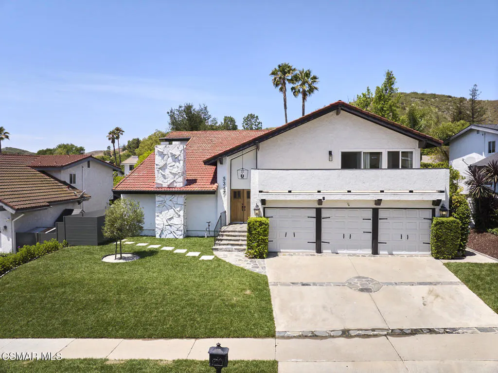 Two-story white house with a red tile roof, three-car garage, and green lawn on a sunny day.