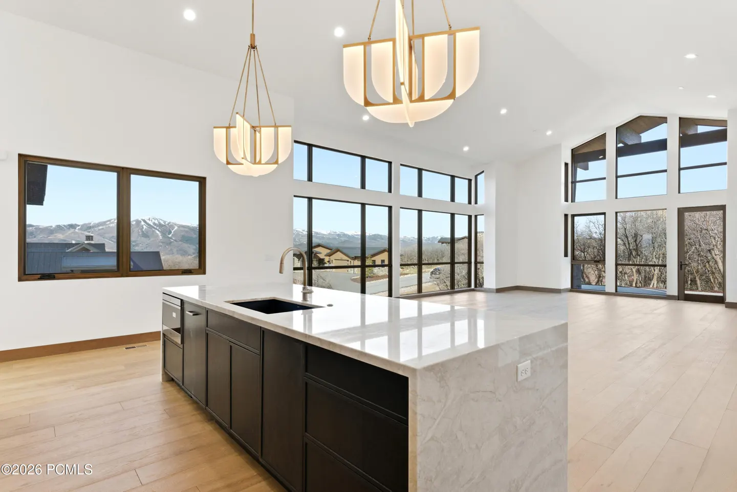 Bright, modern kitchen with a black island, marble countertop, and two pendant lights. Large windows offer mountain views.