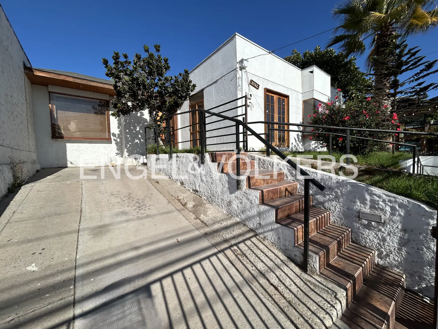 Exterior of a white, two-story house with brown trim, steps, and a ramp leading to the front door. Palm tree and blue sky in the background.
