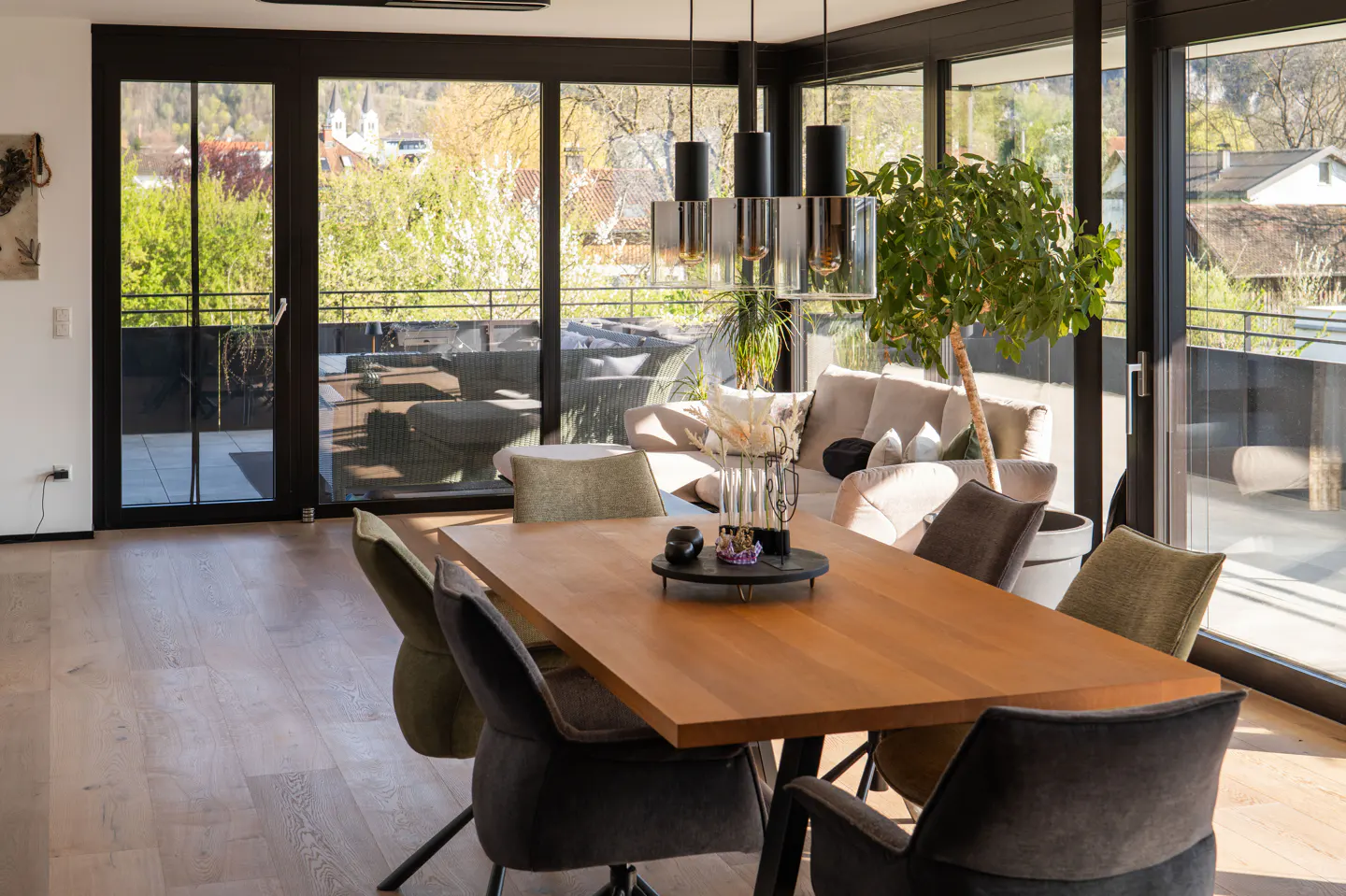Bright dining room with wood table, upholstered chairs, and black-framed glass doors leading to a balcony with outdoor seating.