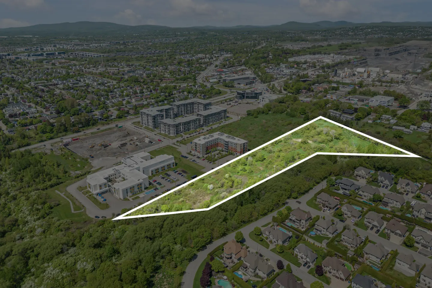 Aerial view of a suburban area with a white outline highlighting a vacant, tree-covered plot of land for development.