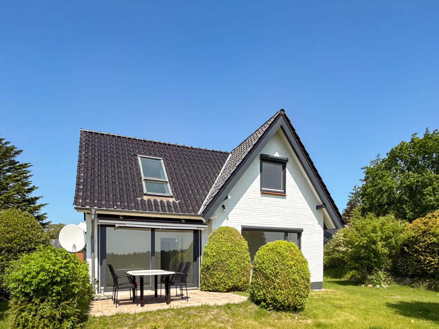 A white brick house with a black roof and a patio with a table and chairs.