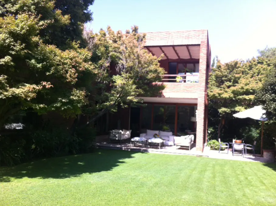Two-story brick house with a patio and green lawn. White outdoor furniture is on the patio. Trees surround the house.