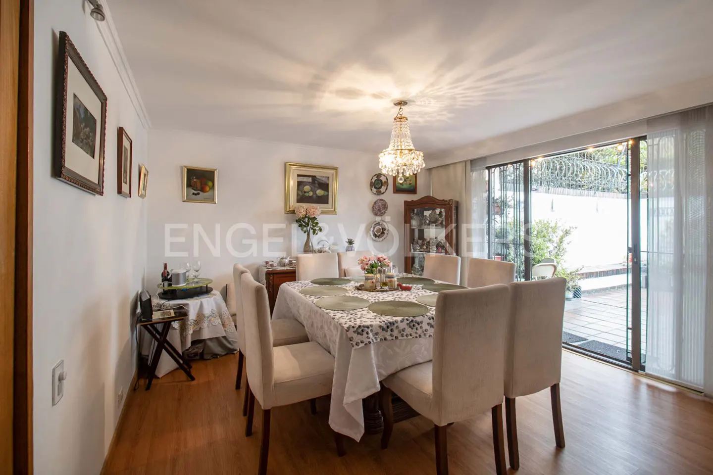 A dining room with a table set for a meal, beige chairs, and a chandelier. Sliding glass doors lead to a patio.
