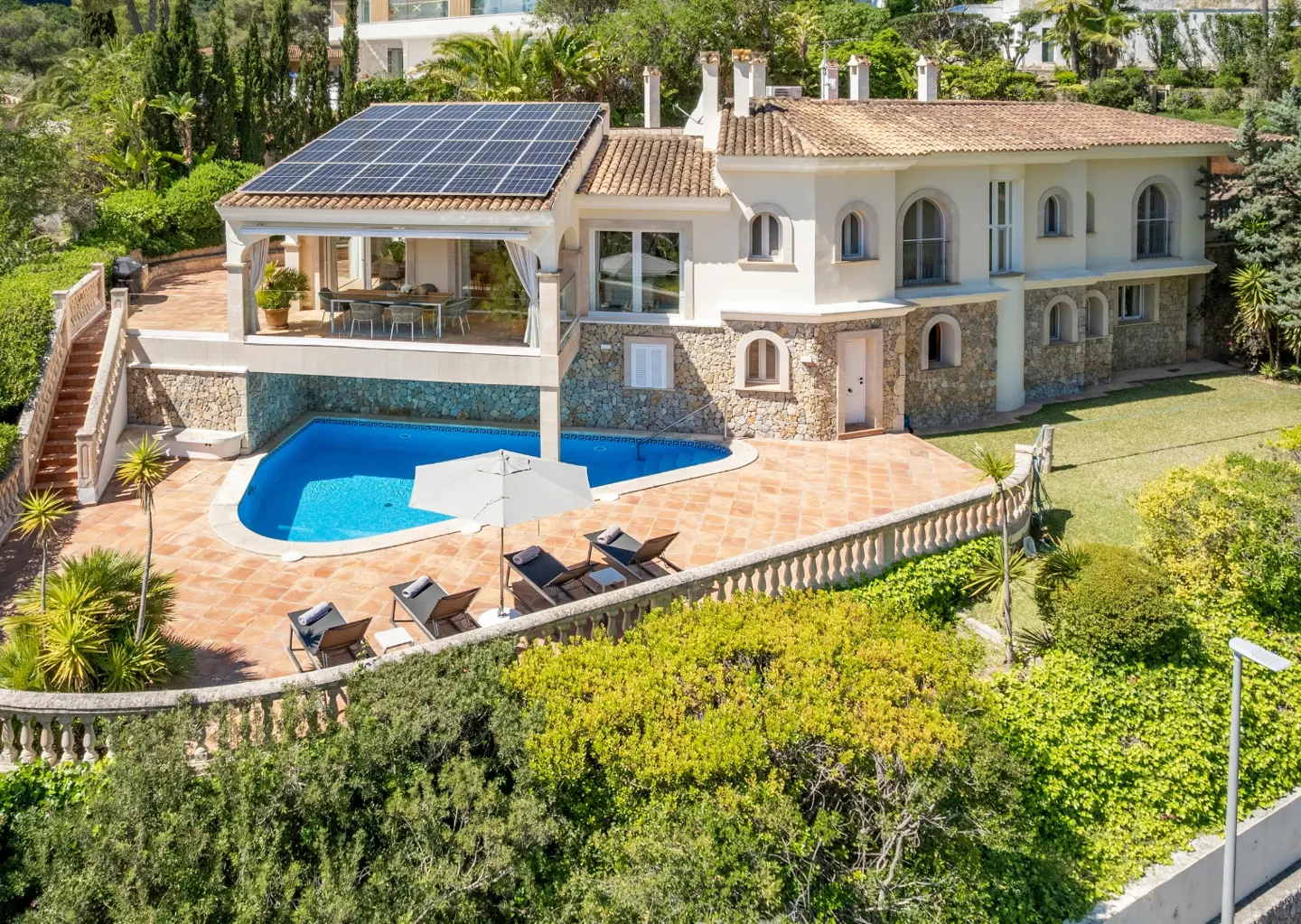 Mediterranean-style villa with a pool, lounge chairs, and solar panels on the roof.