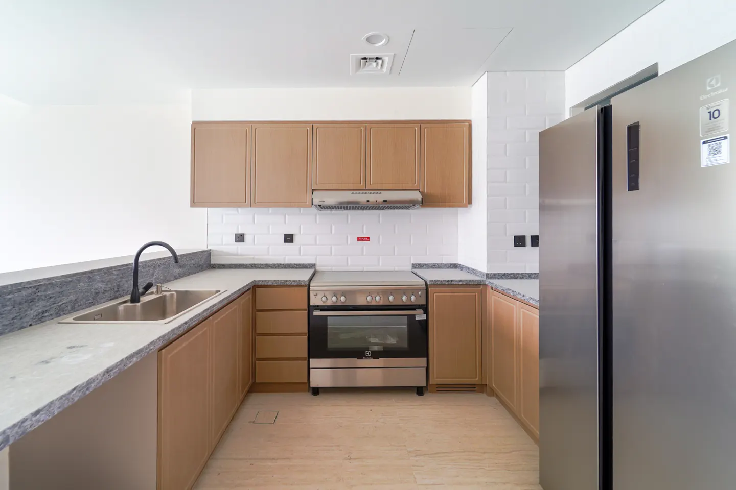 Bright kitchen with stainless steel appliances, light wood cabinets, and white subway tile backsplash. A black faucet sits above a stainless steel sink.