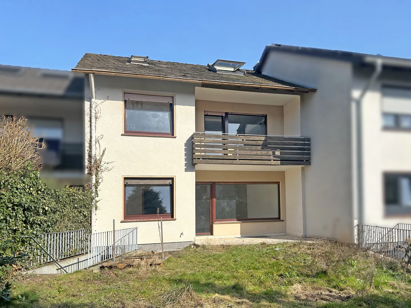 Exterior view of a two-story beige apartment building with a brown balcony and window frames, set against a blue sky.