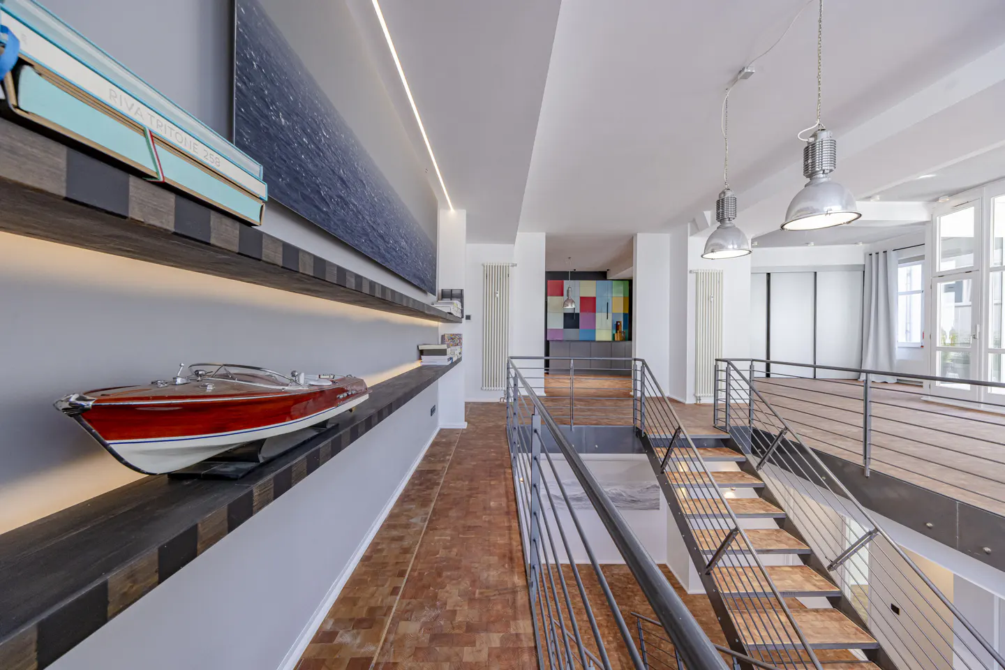 Interior view of a modern home with a staircase, shelves with a boat model, and a colorful wall art in the background.