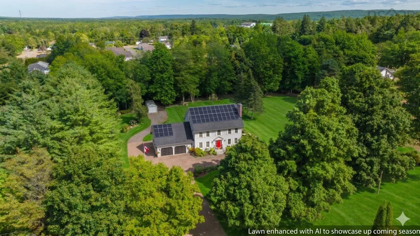 Aerial view of a two-story gray house with a red door, surrounded by green trees and a lawn. Solar panels are installed on the roof.