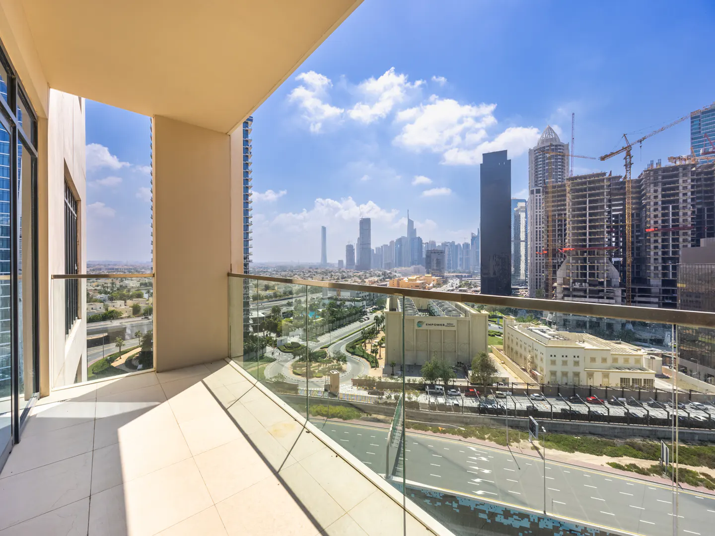 View from a balcony with glass railings overlooking a cityscape with skyscrapers under a blue sky with clouds.