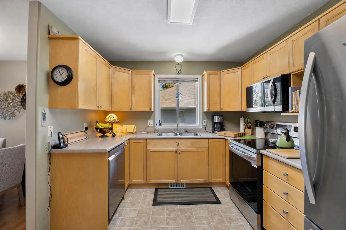 A bright kitchen with light wood cabinets, stainless steel appliances, and a window over the sink.