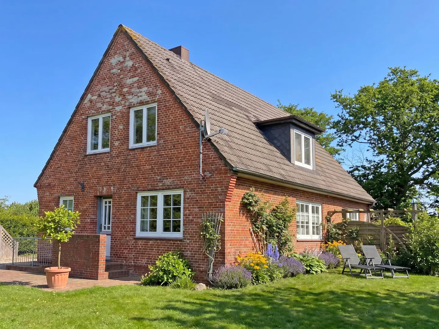 Red brick house with a brown roof, white windows, and green lawn on a sunny day.