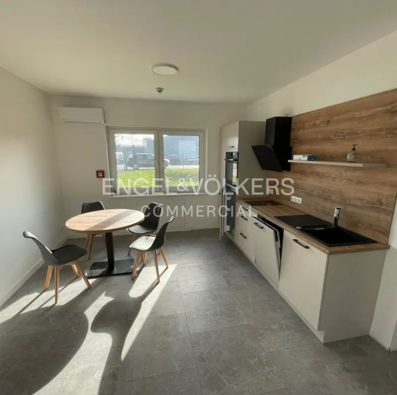 A bright kitchen with a round table, four chairs, and modern cabinets with a black sink and hood.