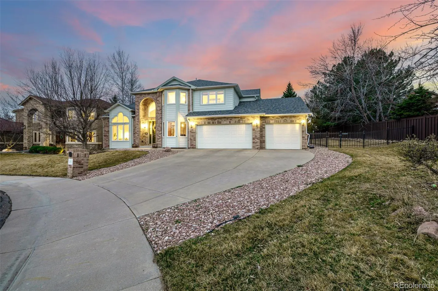 Two-story house with a three-car garage, a concrete driveway, and a lawn at sunset.