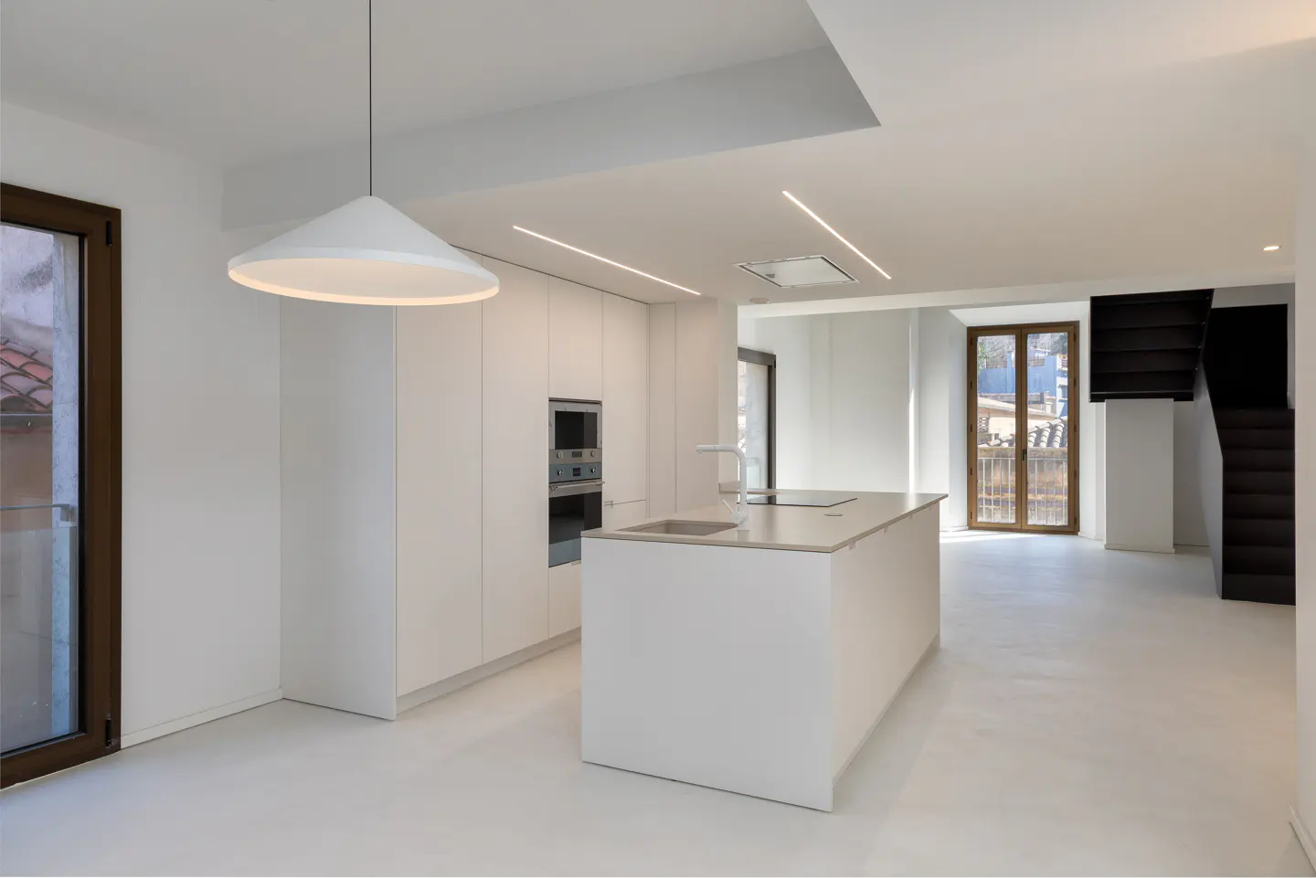 Bright, modern kitchen with white cabinets, island, and floors. A large white pendant light hangs above the island. A staircase is visible in the background.