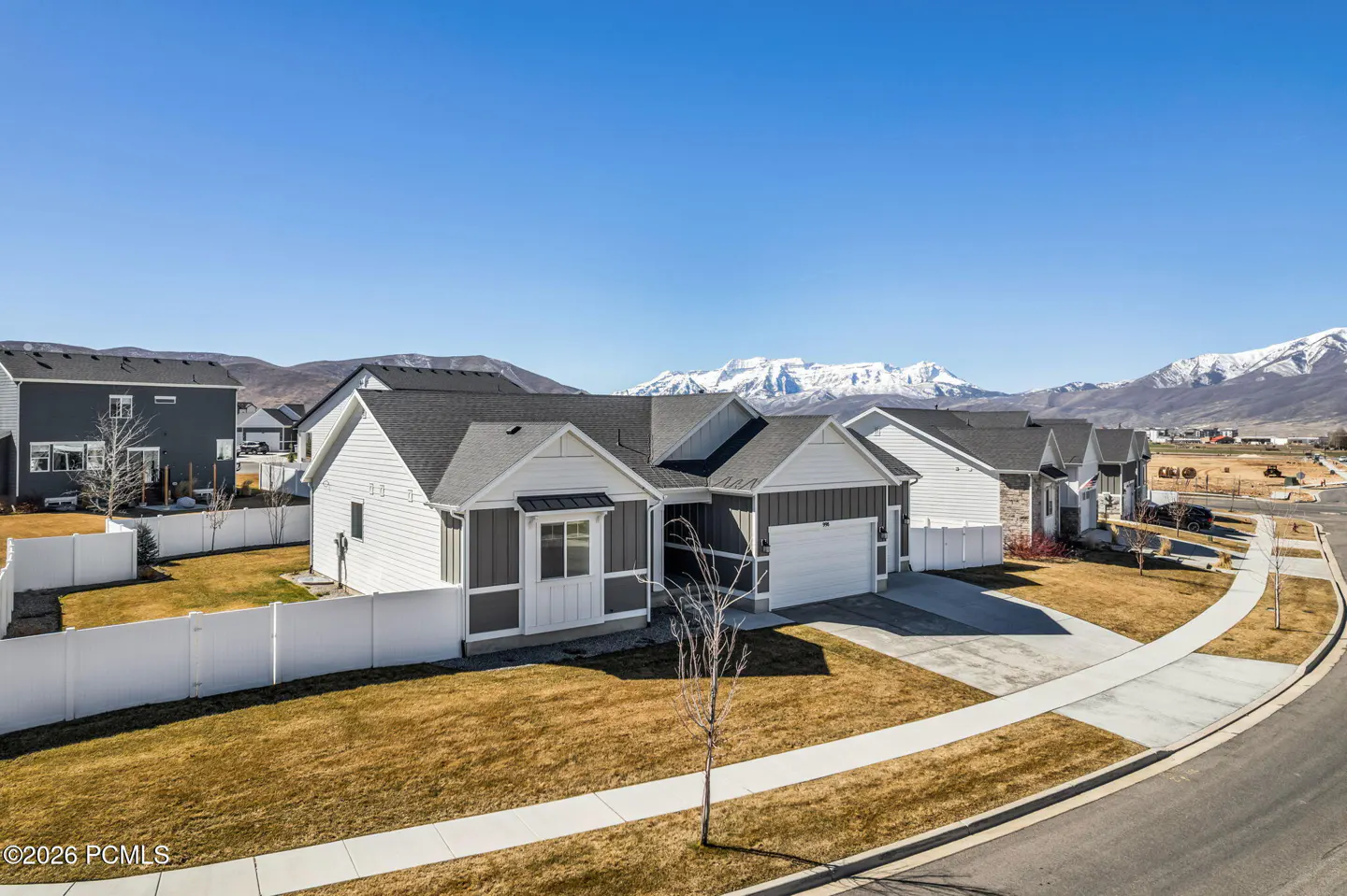 Exterior view of a gray and white single-family home with a two-car garage, lawn, and snow-capped mountains in the background.