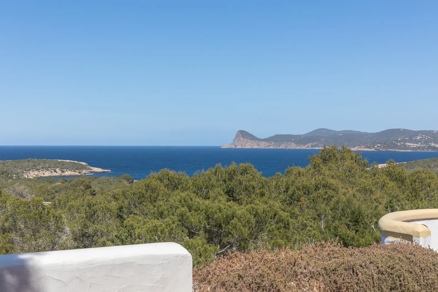 Ocean view from a property, featuring green trees, blue water, islands, and a clear blue sky.